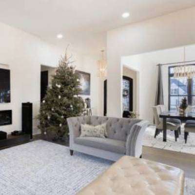 Spacious bathroom with large bathtub, two sinks, wall mirrors, and a cushioned chair. There is a potted plant and towels are hung beside the sinks. Natural light streams through the glass doors.