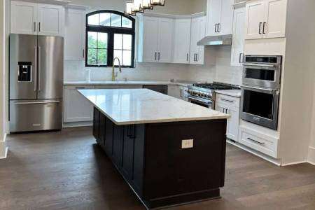 A bathroom with a round mirror, two orange towels, a black faucet with a brown vessel sink, and soap dispensers. A doorway leads to a room with a dresser and lamp.