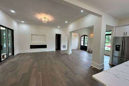 A kitchen under renovation with incomplete cabinetry, dark wood upper cabinets, and white lower cabinets. A ladder and some tools are visible, and large windows provide natural light.