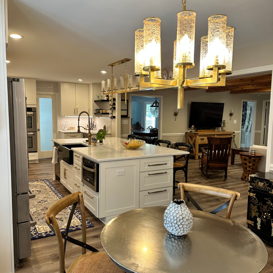 Modern kitchen and dining area with white cabinetry, island, stainless steel appliances, round table, decorative vase, and gold chandelier lighting.