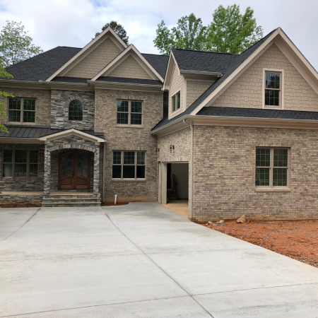 Two-story brick house with a double front door, attached garage, multiple windows, and a large concrete driveway.