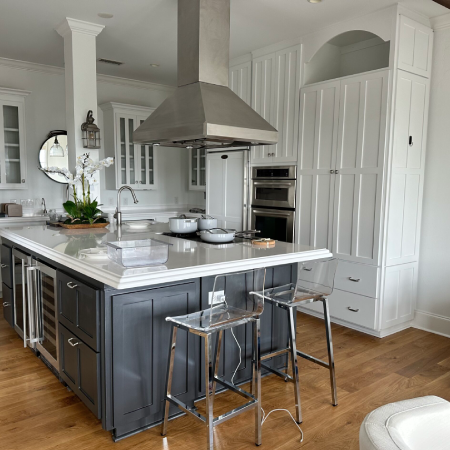 Modern kitchen with a large island, gray cabinets, stainless steel appliances, glass stools, and white cabinetry. An orchid plant sits on the island countertop.